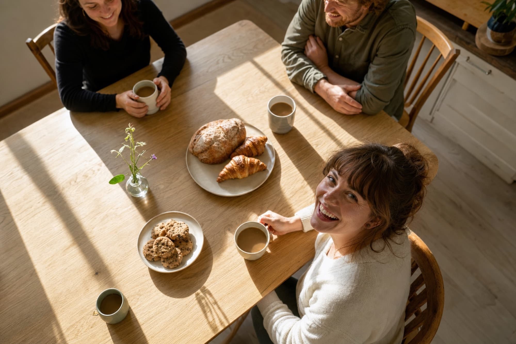 A sunny table with coffee, pastries, and people laughing together