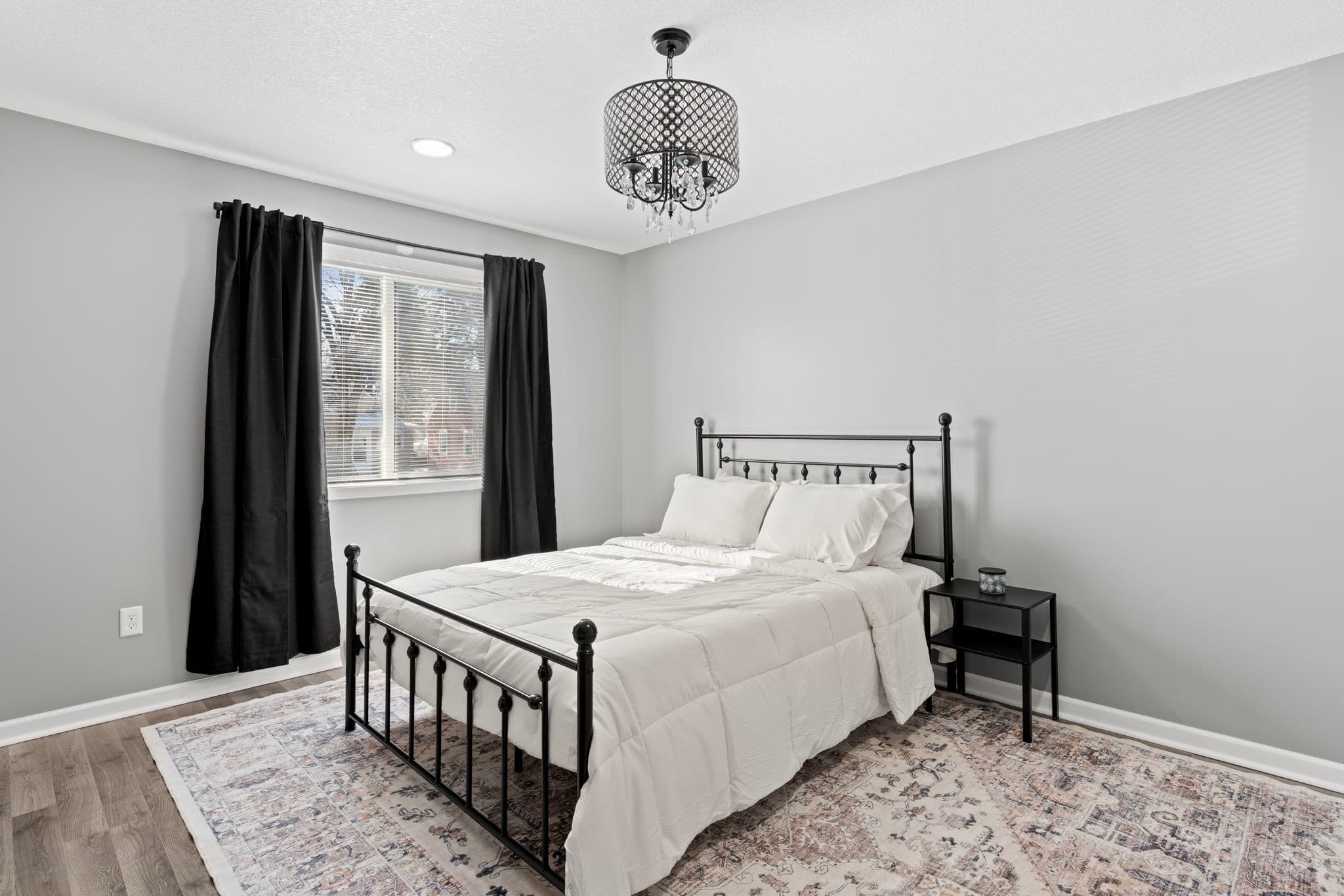 Main-level bedroom with black metal bed, white bedding, and drum crystal chandelier