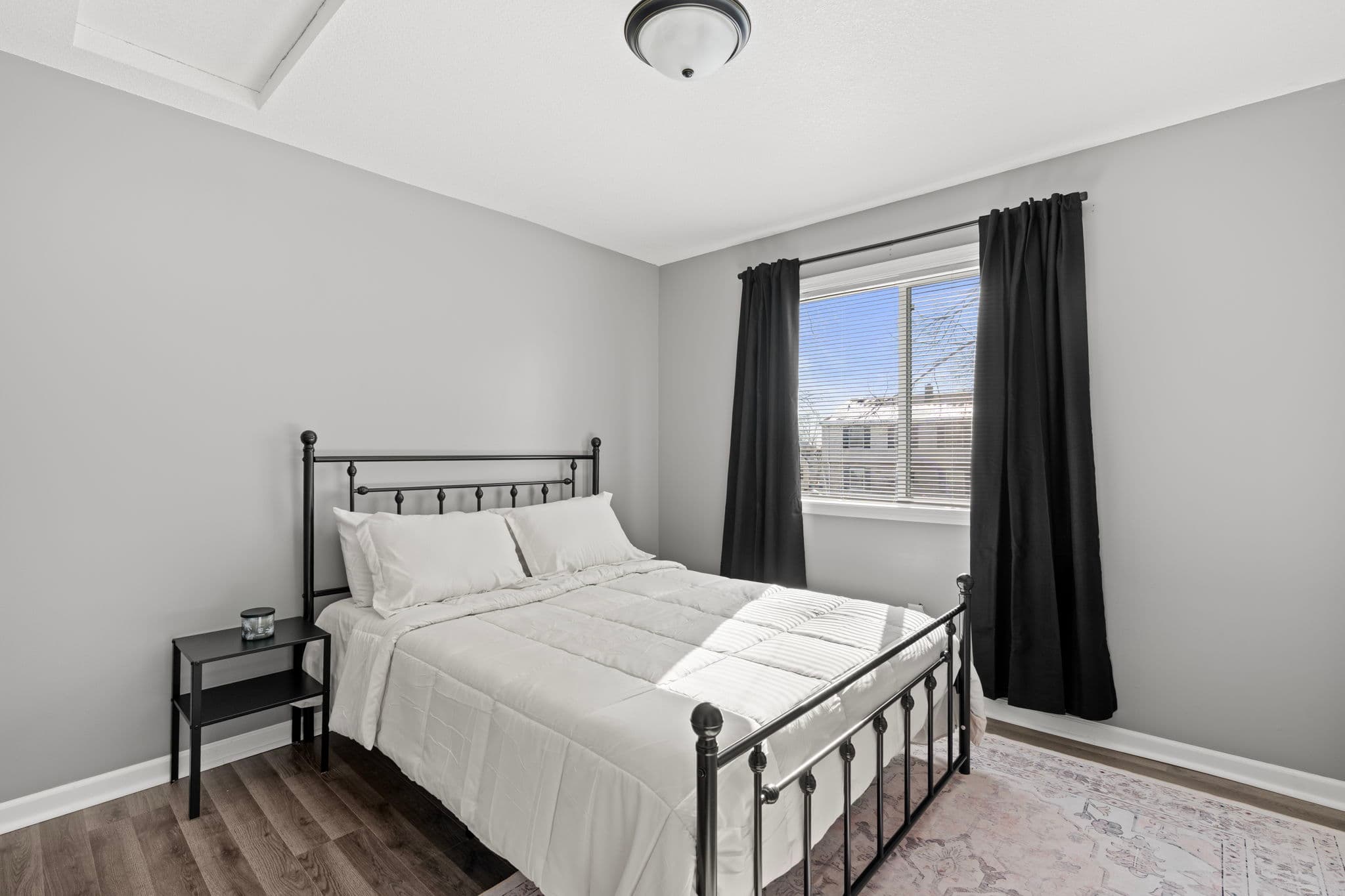 Second main-level bedroom with black metal bed and white comforter