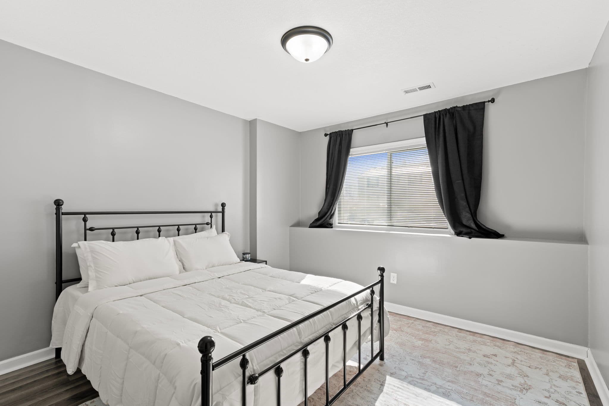 Lower-level bedroom with black metal bed and deep-silled daylight window