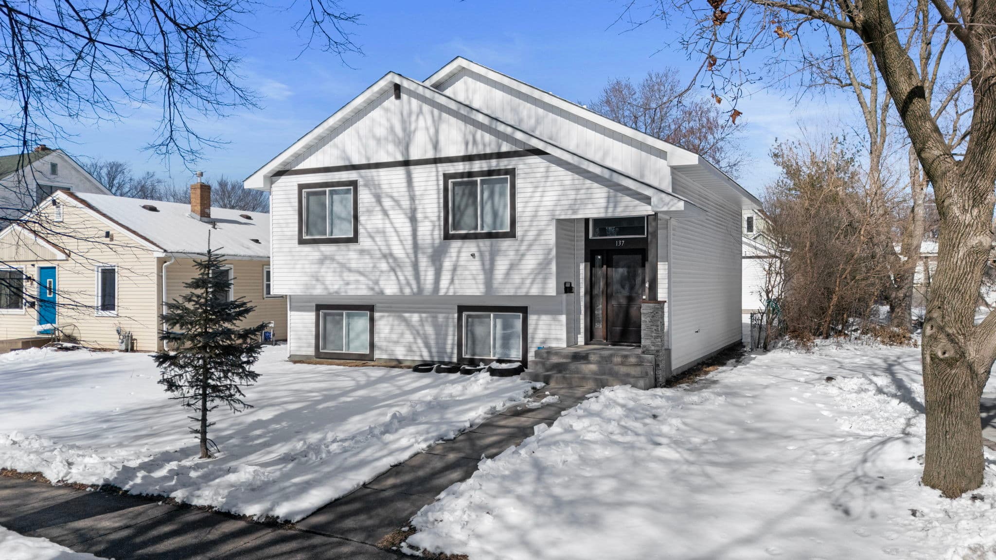 Front of the white split-level home with covered entry, stone-accent pillar, and shoveled walkway