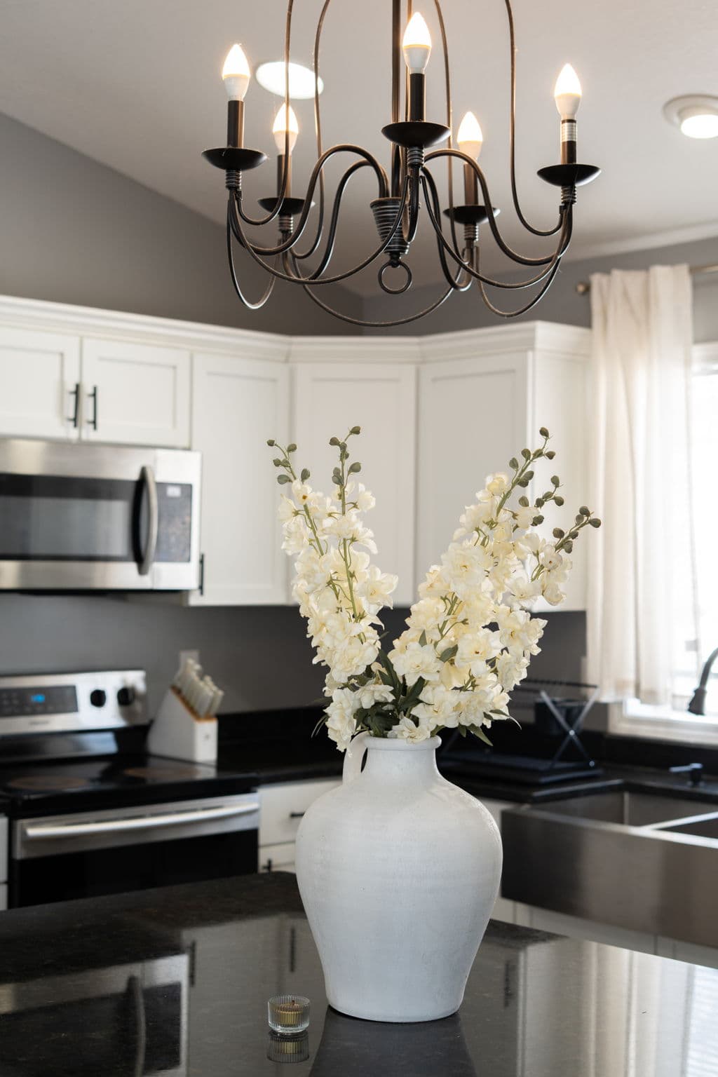 White ceramic vase of flowers on the kitchen island beneath the chandelier