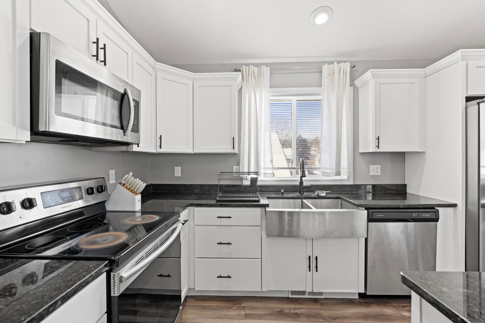 Stainless farmhouse sink with black gooseneck faucet under a curtained window