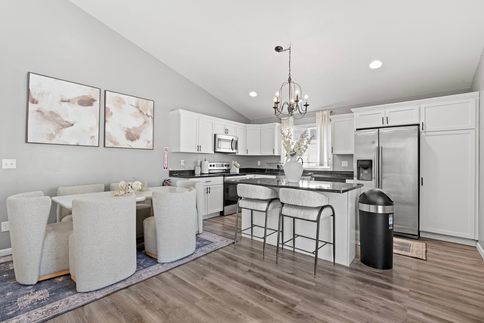 Open kitchen with white cabinets, dark granite counters, stainless fridge, and island with stools