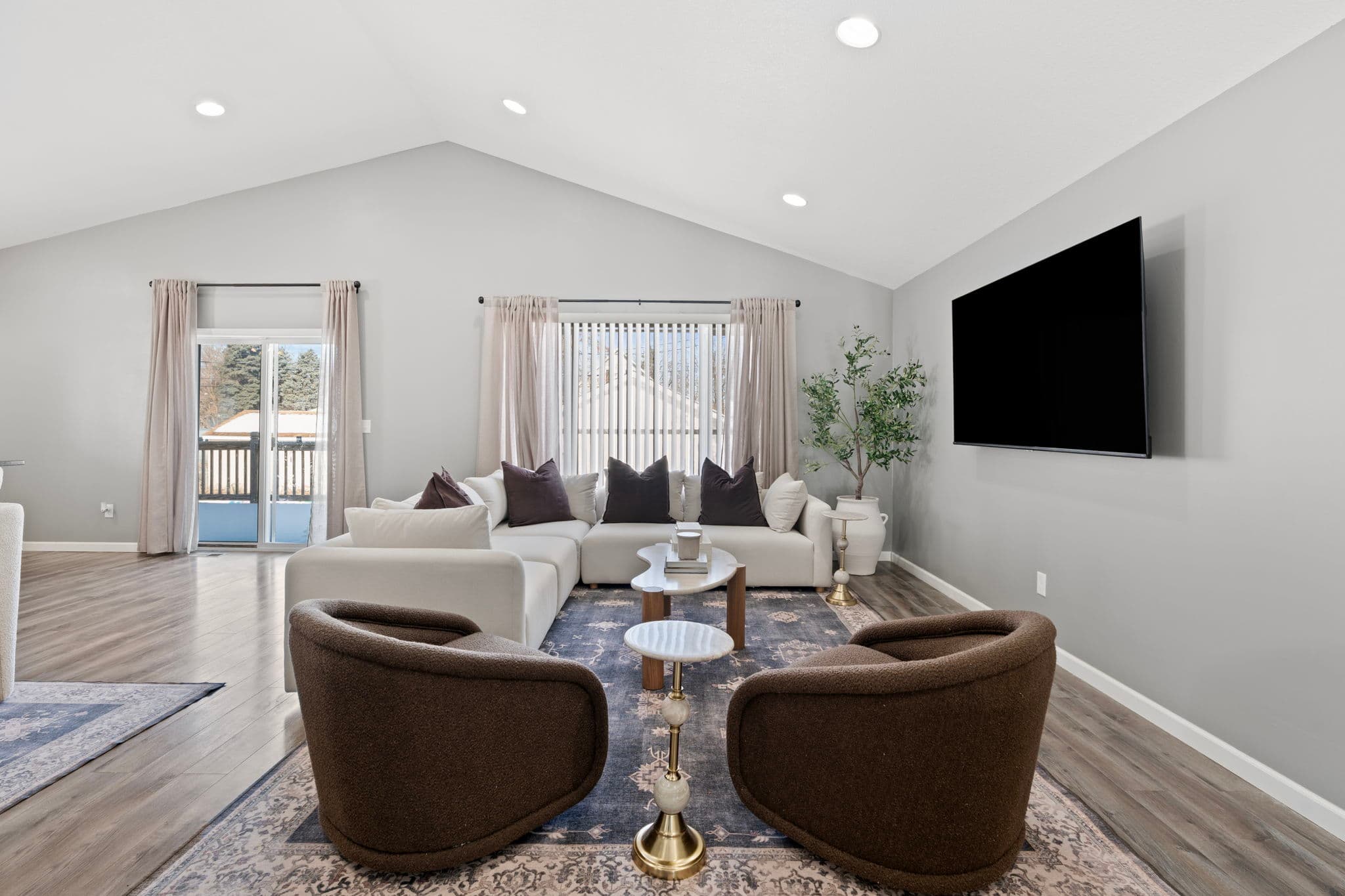 Vaulted-ceiling living room with white sectional, swivel chairs, wall-mounted TV, and sliding door to the deck