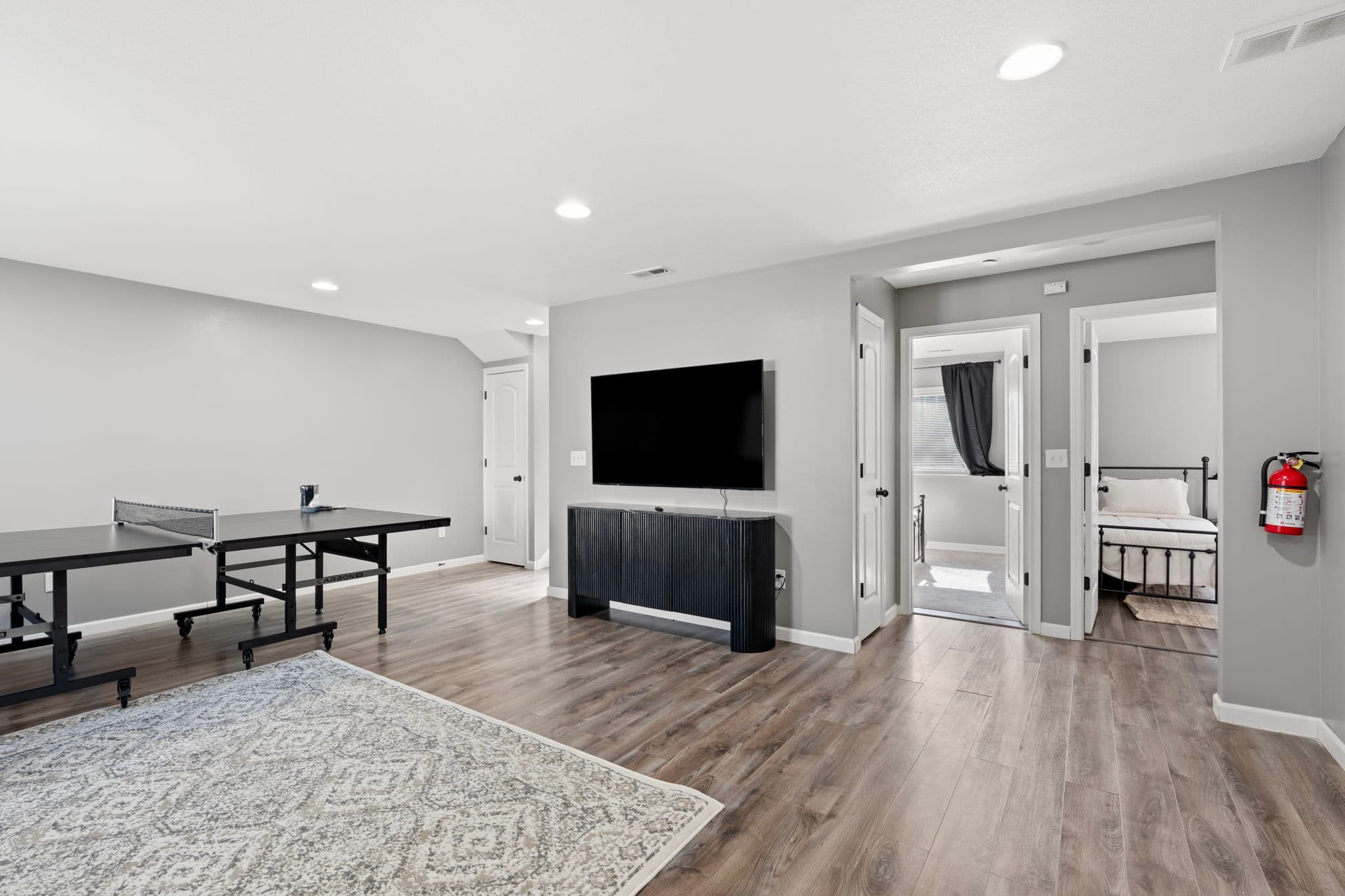Rec room with wall-mounted TV, ping-pong table, and doorways to two bedrooms