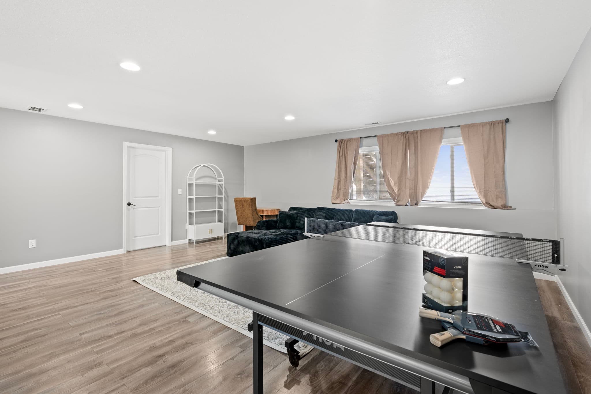 Lower-level rec room with ping-pong table, black sectional, and arched white bookshelf